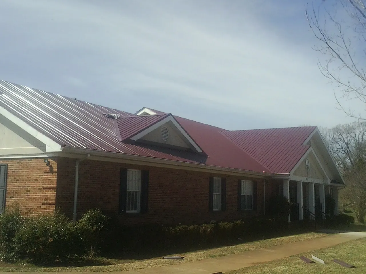 Red metal roof with gabled entries on a long brick building, from a Hail Damage Roof Repair job in Radcliff