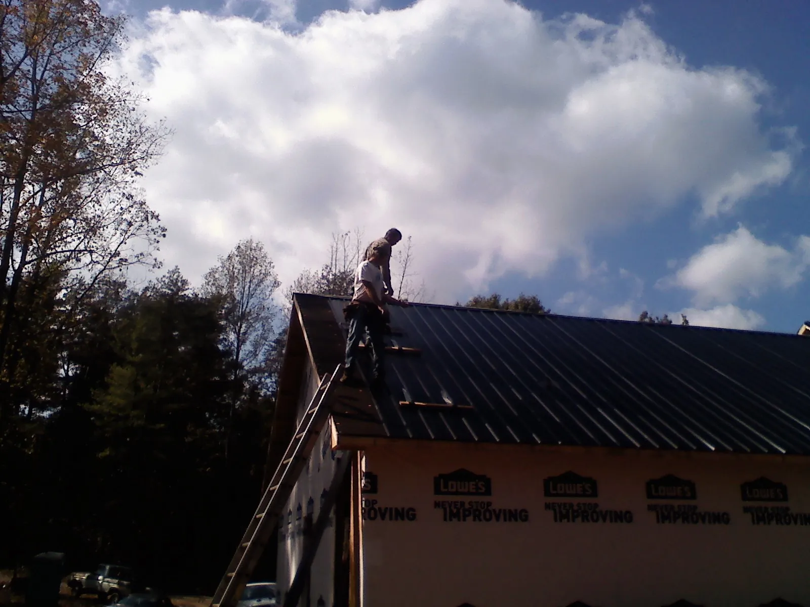 Roofer fastening dark metal panels high against a cloudy sky, from a Roof Inspection job in Radcliff