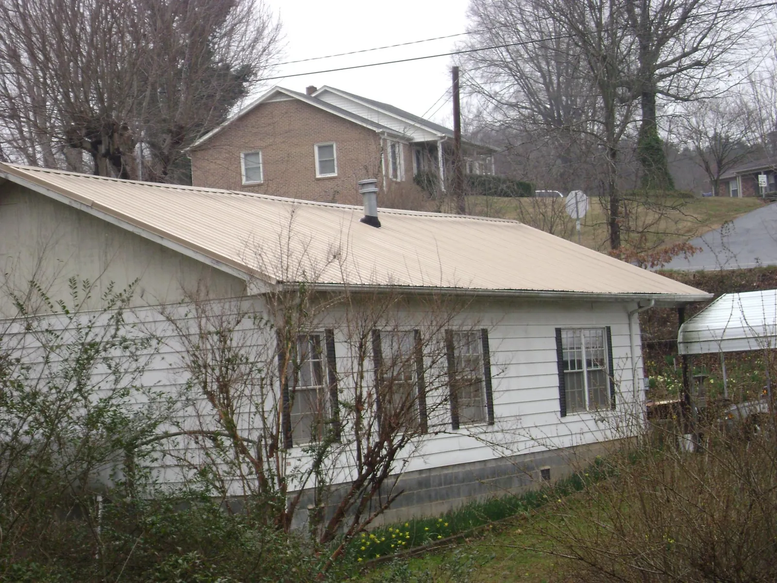 Tan metal roof on a white sided house set into a hillside — Commercial Roofing by Roofing Brothers in Radcliff