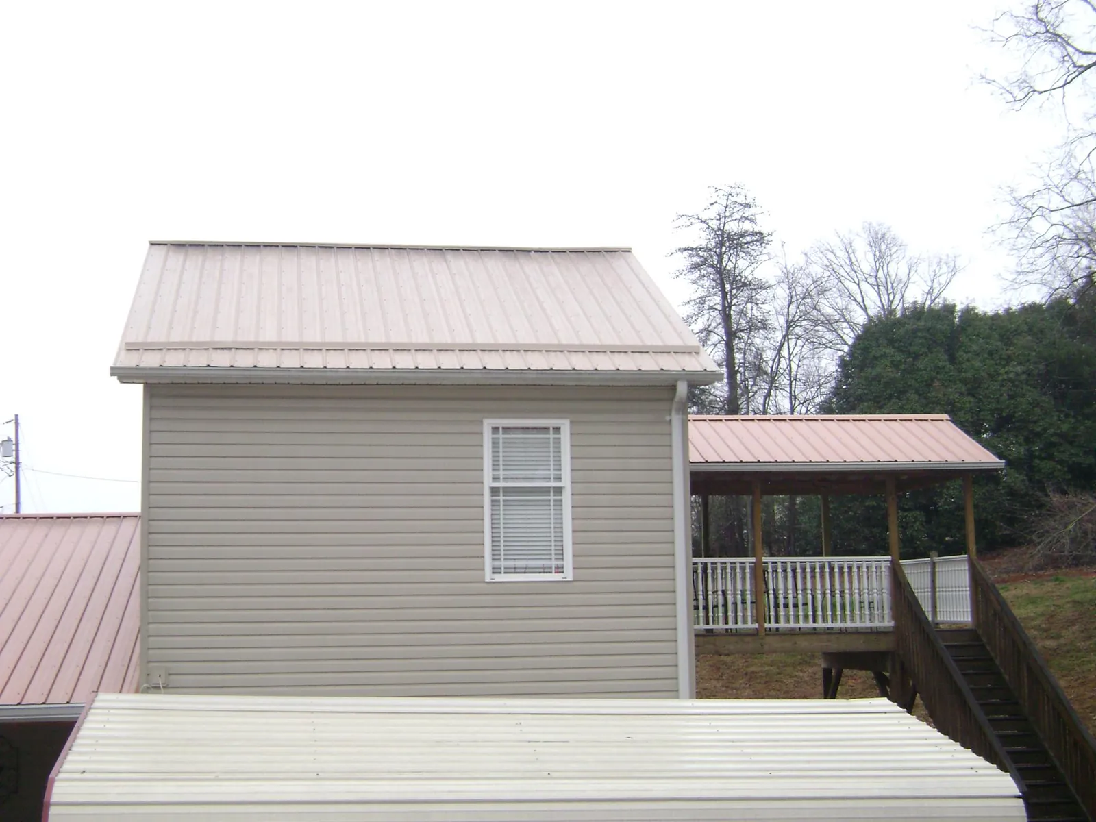 Tan metal roofs on a two story addition and attached porch, from a Roof Replacement job in Radcliff